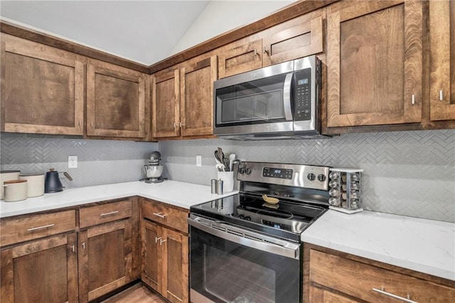 12631 Fountain Lake Cir, Grandview, MO 64030 - kitchen with stainless steel appliances, tasteful backsplash, lofted ceiling, light stone counters, and brown cabinets