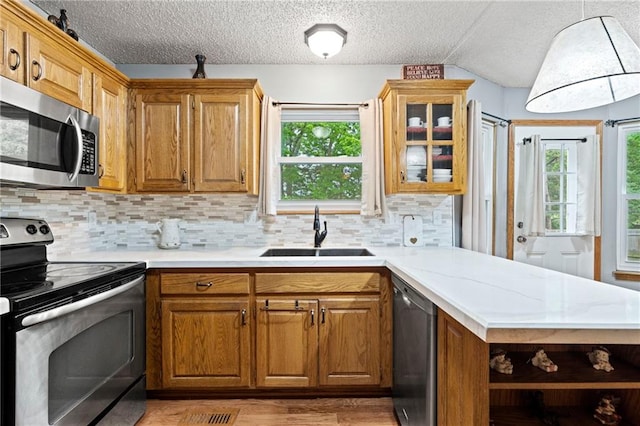 kitchen with open shelves, a sink, light wood-style floors, stainless steel appliances, and decorative backsplash