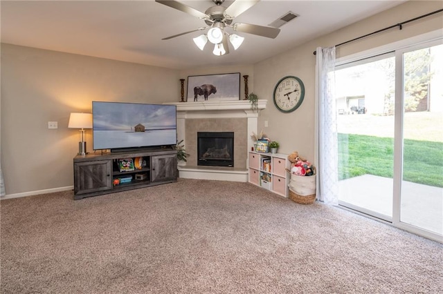 living area featuring a tiled fireplace, visible vents, carpet flooring, and a ceiling fan