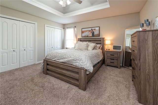 bedroom featuring a raised ceiling, ornamental molding, carpet floors, two closets, and ceiling fan