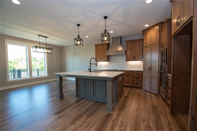 kitchen with dark wood-style flooring, custom exhaust hood, a sink, brown cabinets, and a kitchen island with sink