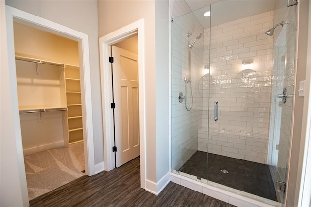 full bathroom featuring a stall shower, baseboards, a walk in closet, and wood finished floors