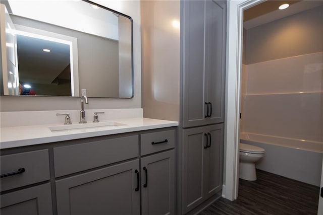 full bath featuring toilet, wood finished floors, vanity, shower / bathing tub combination, and recessed lighting