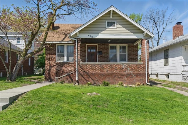 bungalow-style house with a front lawn, brick siding, and a chimney
