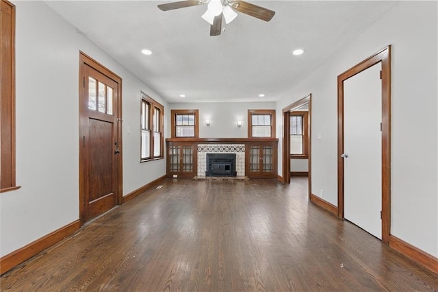 unfurnished living room featuring baseboards, a brick fireplace, a healthy amount of sunlight, and dark wood finished floors