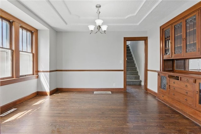 unfurnished room featuring stairway, a raised ceiling, wood finished floors, visible vents, and a notable chandelier