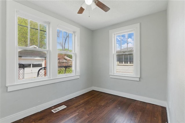 spare room featuring baseboards, dark wood-type flooring, visible vents, and plenty of natural light
