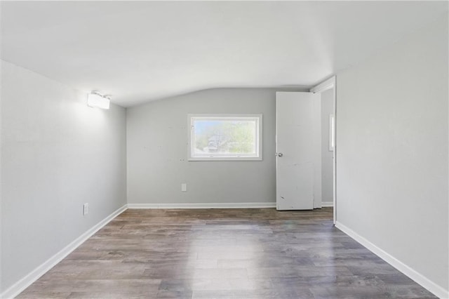 spare room with baseboards, vaulted ceiling, and wood finished floors