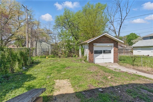 view of yard featuring a detached garage, an outbuilding, concrete driveway, and fence