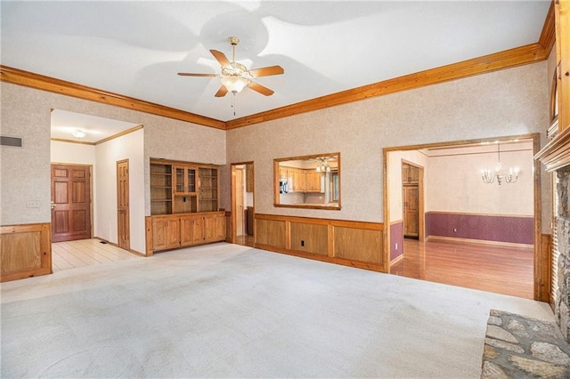unfurnished living room featuring crown molding, a wainscoted wall, vaulted ceiling, carpet, and ceiling fan with notable chandelier