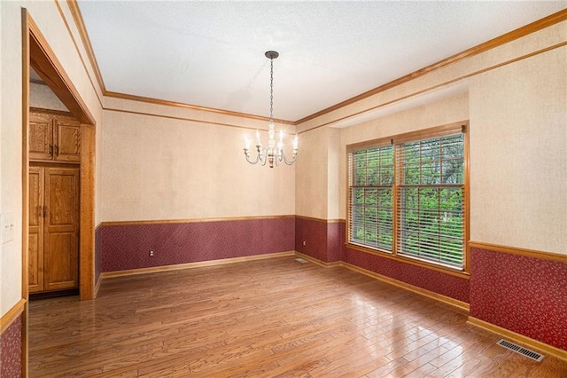 spare room featuring a chandelier, wallpapered walls, ornamental molding, wood-type flooring, and visible vents