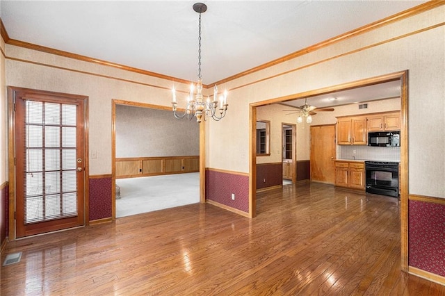 unfurnished dining area featuring hardwood / wood-style floors, wainscoting, ceiling fan with notable chandelier, visible vents, and crown molding