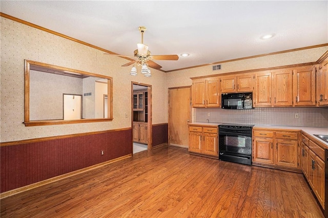 kitchen featuring black appliances, wood finished floors, a wainscoted wall, and light countertops
