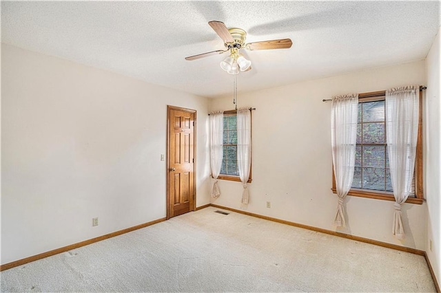 carpeted spare room featuring a textured ceiling, visible vents, ceiling fan, and baseboards