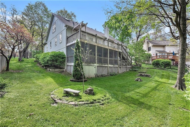 back of property with a chimney, a balcony, a sunroom, and a lawn