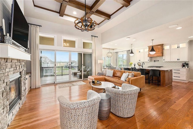 living area featuring beam ceiling, a notable chandelier, coffered ceiling, a high ceiling, and a stone fireplace