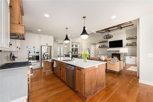 kitchen with a stone fireplace, a sink, light countertops, appliances with stainless steel finishes, and recessed lighting