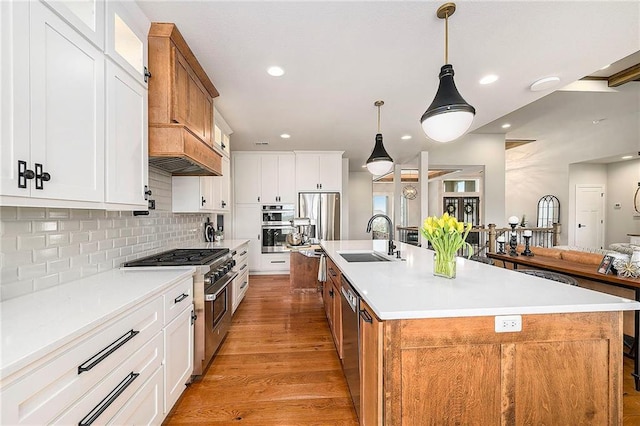 kitchen featuring stainless steel appliances, a large island with sink, a sink, light wood-type flooring, and backsplash
