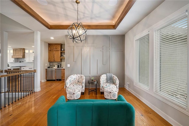 sitting room featuring light wood-type flooring, baseboards, a tray ceiling, and an inviting chandelier
