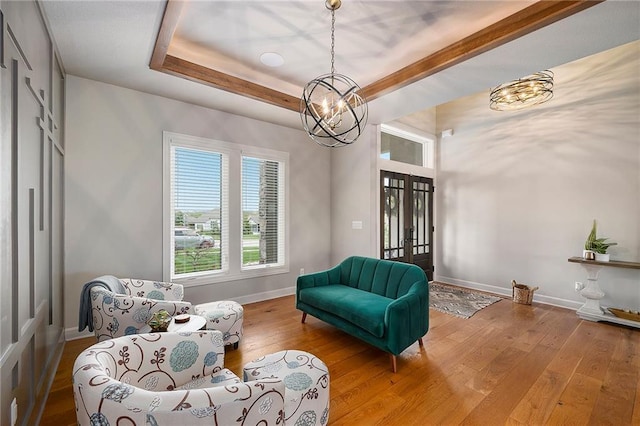 living area featuring a tray ceiling, french doors, baseboards, hardwood / wood-style flooring, and a notable chandelier