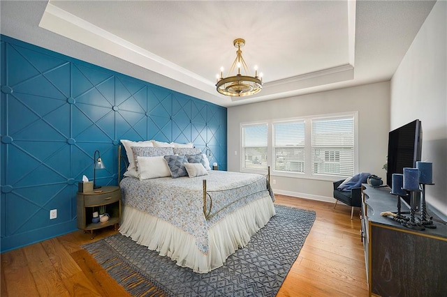 bedroom with an accent wall, hardwood / wood-style floors, an inviting chandelier, a raised ceiling, and baseboards
