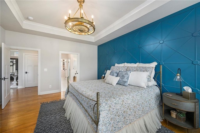 bedroom featuring a raised ceiling, wood finished floors, baseboards, and an inviting chandelier