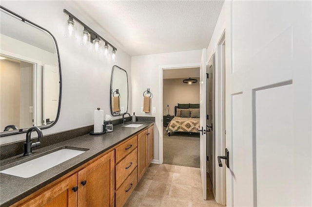 bathroom featuring a textured ceiling, double vanity, connected bathroom, and a sink