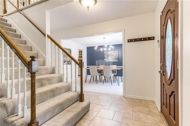 entrance foyer with stairway, baseboards, a chandelier, and stone finish floors