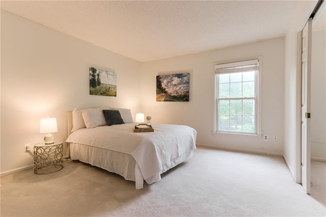 bedroom featuring light colored carpet, baseboards, and a textured ceiling