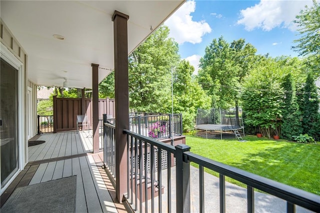 wooden deck featuring a trampoline, a yard, and view of scattered trees