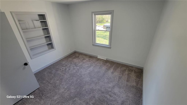carpeted empty room featuring built in shelves and baseboards