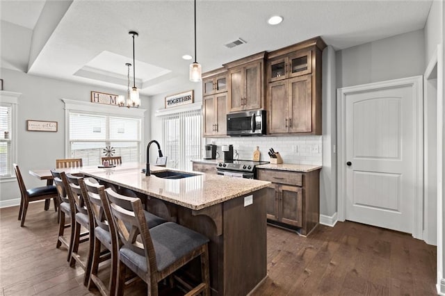1002 Fox Trot Dr, Odessa, MO 64076 - kitchen with stainless steel appliances, a sink, tasteful backsplash, dark wood-style floors, and a center island with sink
