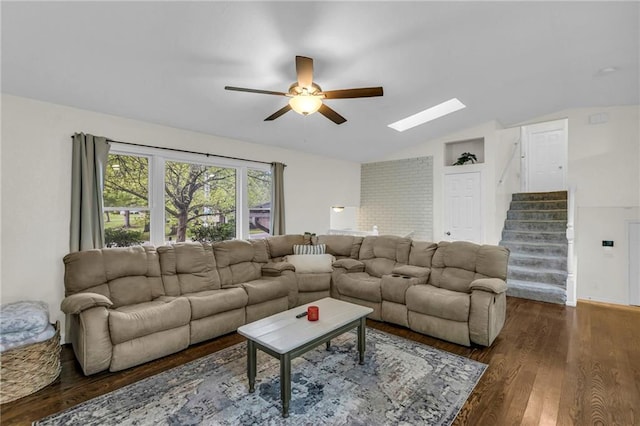 living room featuring vaulted ceiling with skylight, a ceiling fan, stairs, and dark wood-type flooring