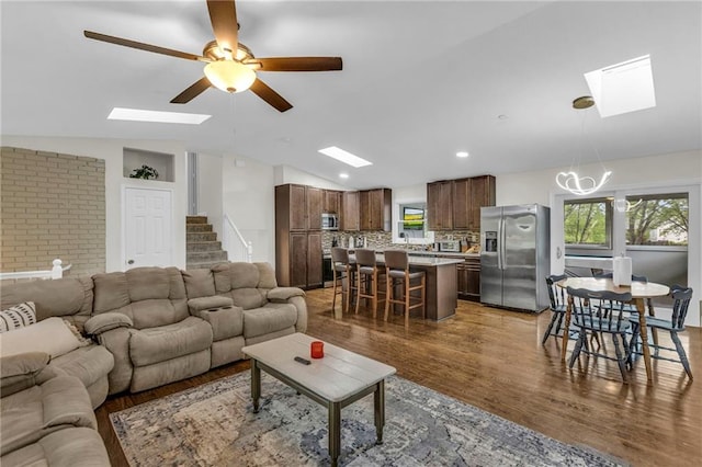 living room featuring plenty of natural light, ceiling fan with notable chandelier, lofted ceiling with skylight, and wood finished floors