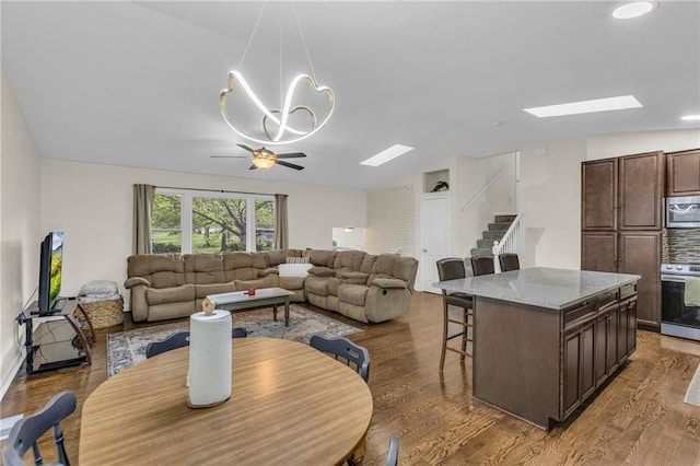 living area featuring a ceiling fan, lofted ceiling with skylight, and wood finished floors