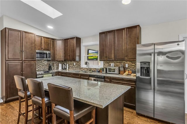 kitchen with a sink, a breakfast bar area, wood finished floors, and stainless steel appliances