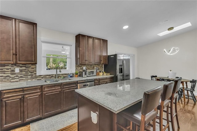 kitchen featuring a breakfast bar, light wood-type flooring, a sink, backsplash, and stainless steel appliances
