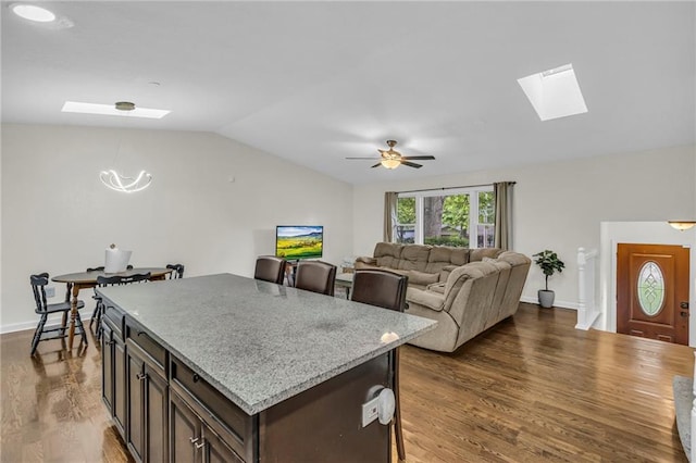 kitchen featuring dark brown cabinetry, dark wood-style flooring, a center island, baseboards, and lofted ceiling with skylight