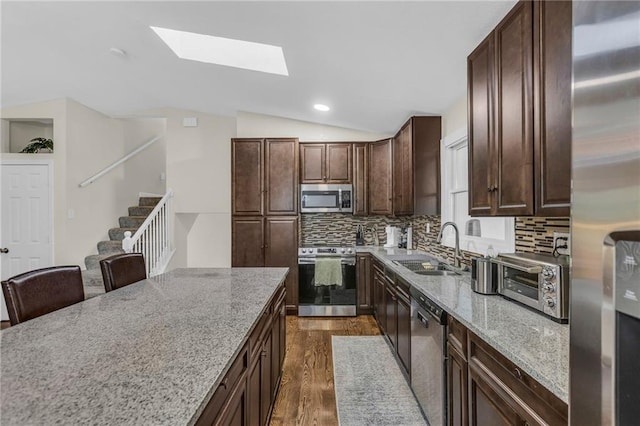 kitchen with a toaster, dark wood-type flooring, vaulted ceiling with skylight, a sink, and stainless steel appliances