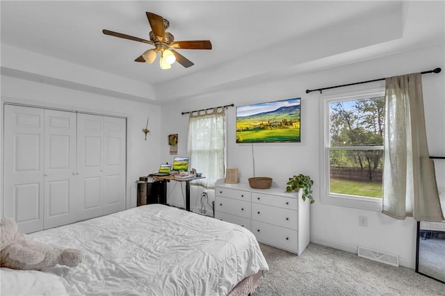 bedroom with visible vents, a closet, light carpet, a raised ceiling, and a ceiling fan