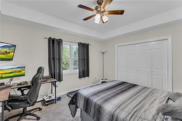 carpeted bedroom featuring a tray ceiling, baseboards, a ceiling fan, and a closet