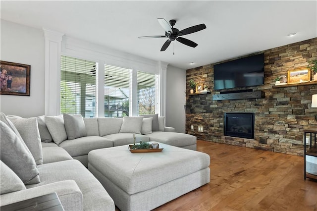 living area with a ceiling fan, wood finished floors, and a stone fireplace