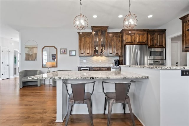 kitchen with stainless steel appliances, a breakfast bar, recessed lighting, decorative backsplash, and glass insert cabinets