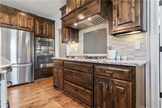 kitchen featuring stainless steel appliances, dark brown cabinets, decorative backsplash, and light wood finished floors