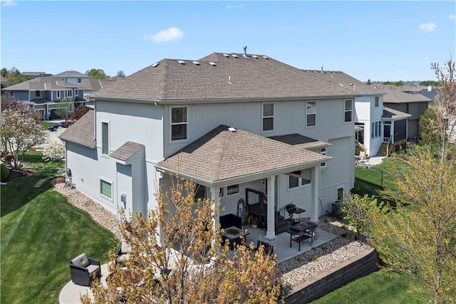 rear view of property featuring a shingled roof, a patio area, a residential view, and a lawn