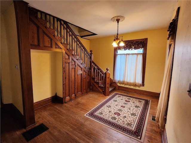 entrance foyer with wood finished floors, a notable chandelier, visible vents, and stairs