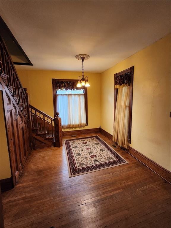 interior space with baseboards, stairway, hardwood / wood-style flooring, and an inviting chandelier
