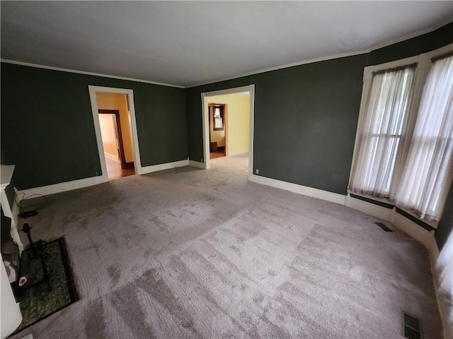 carpeted spare room with baseboards, ornamental molding, and visible vents