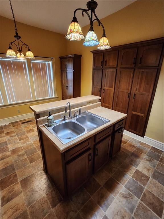 kitchen with stone finish floor, a center island with sink, light countertops, and a sink