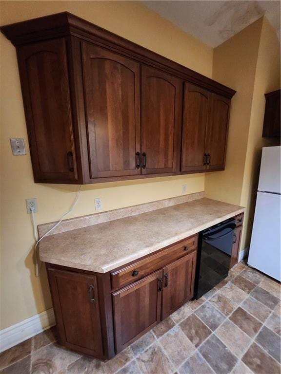 kitchen with freestanding refrigerator, stone finish floor, dishwasher, light countertops, and baseboards